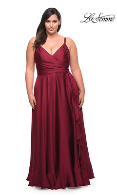 A woman models the Long Plus-Size La Femme Prom Dress, featuring a sleeveless, floor-length burgundy design with a V-neckline and ruffle hem, against a plain white background. The La Femme logo appears in the top right corner.
